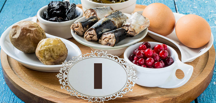 Products containing iodine (seaweed, boiled eggs, cranberries, sardines, baked potatoes, prunes) on a round cutting board and a blue wooden background