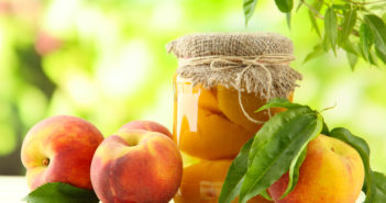 Jar of canned peaches and fresh peaches on wooden table, outside